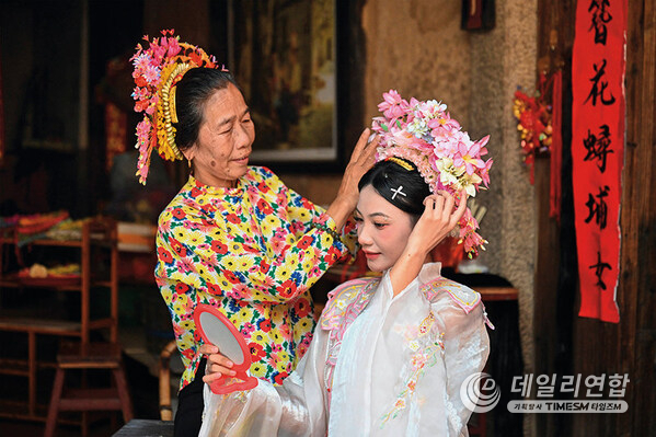 A tourist (right) is wearing flowery headwear at Xunpu Village of Quanzhou City, southeast China's Fujian Province, Aug. 27, 2025. (Provided by Zhou Yi) A tourist (right) is wearing flowery headwear at Xunpu Village of Quanzhou City, southeast China's Fujian Province, Aug. 27, 2025. (Provided by Zhou Yi)